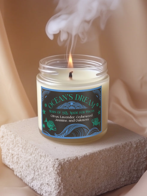 A 9 oz white soy candle in clear glass jar with blue and turquoise oceanic label featuring wave patterns and fish motifs, titled "Ocean's Dream" with a lit cotton wick.